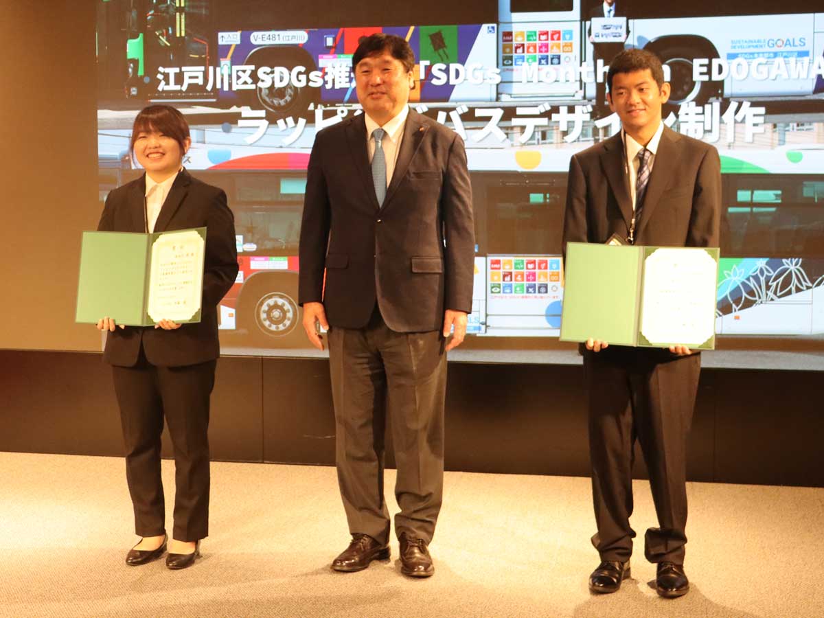 江戸川区SDGs推進部によるラッピングバスデザインの授賞式。江戸川区の斉藤猛区長と、最優秀賞を受賞した長谷川さん（左）と前田さん（右）