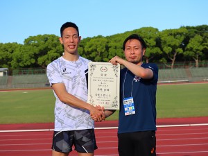 4位入賞の表彰状を掲げて握手する高田先生と高橋選手